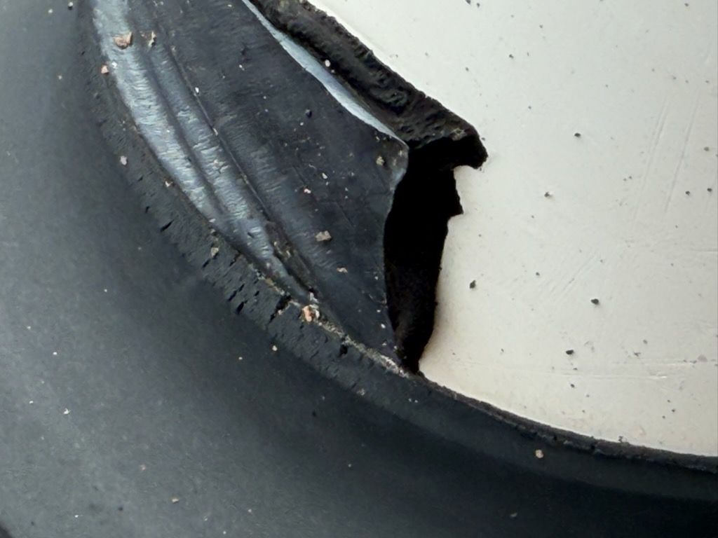 Close-up of a black rubber or plastic edge torn and peeling away from a white surface.