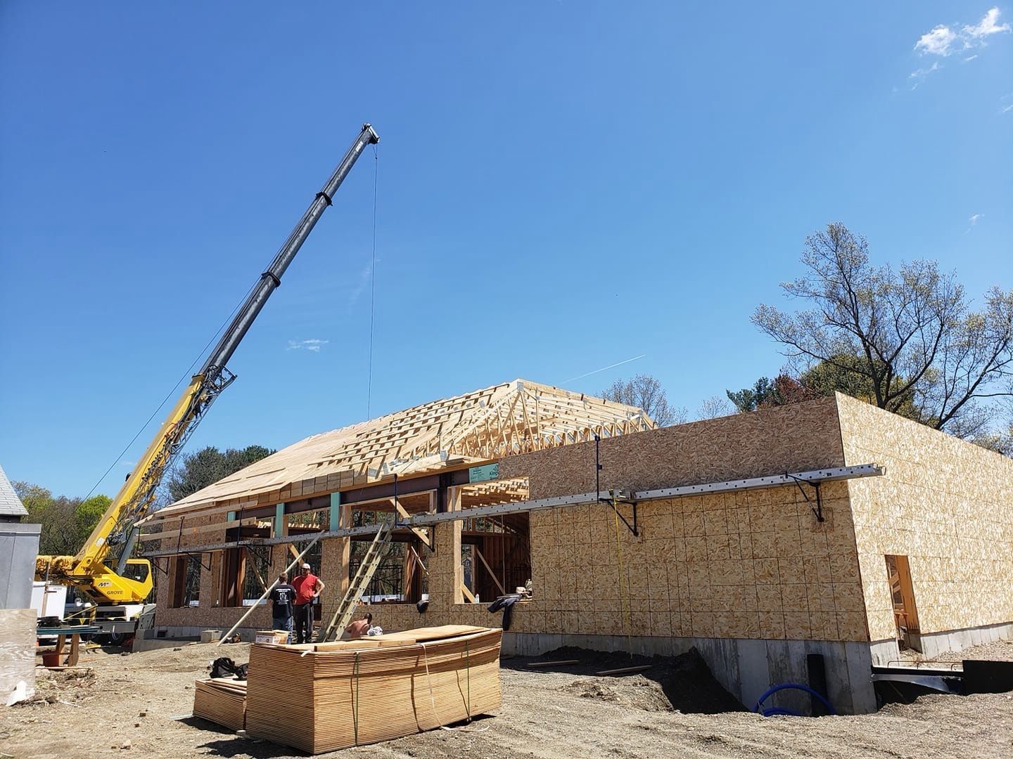 Workers installing roofing on a white house under a blue sky with clouds.