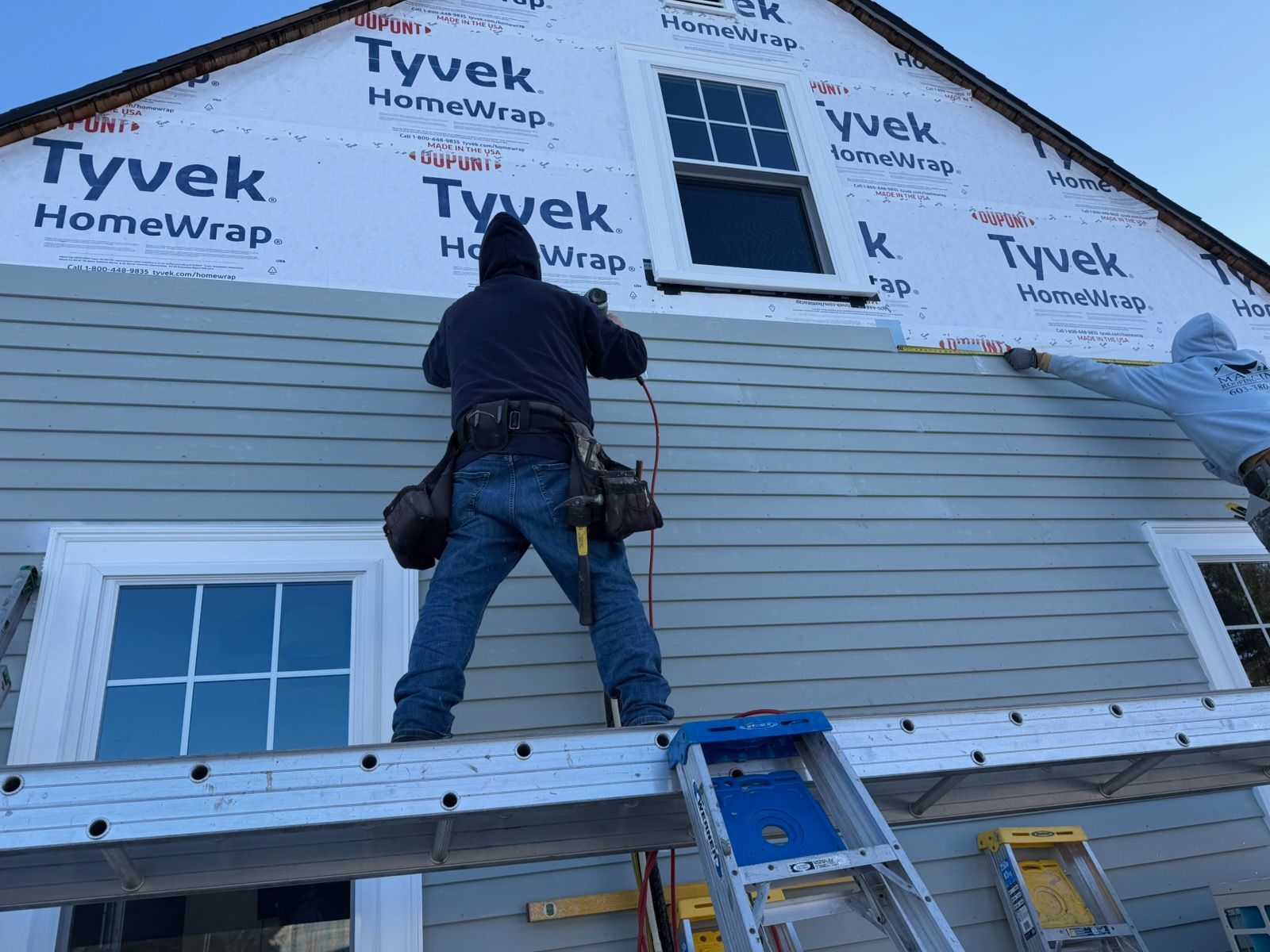 Exterior of a building with blue door, gray siding, white trim, and a snowy yard under a blue sky.