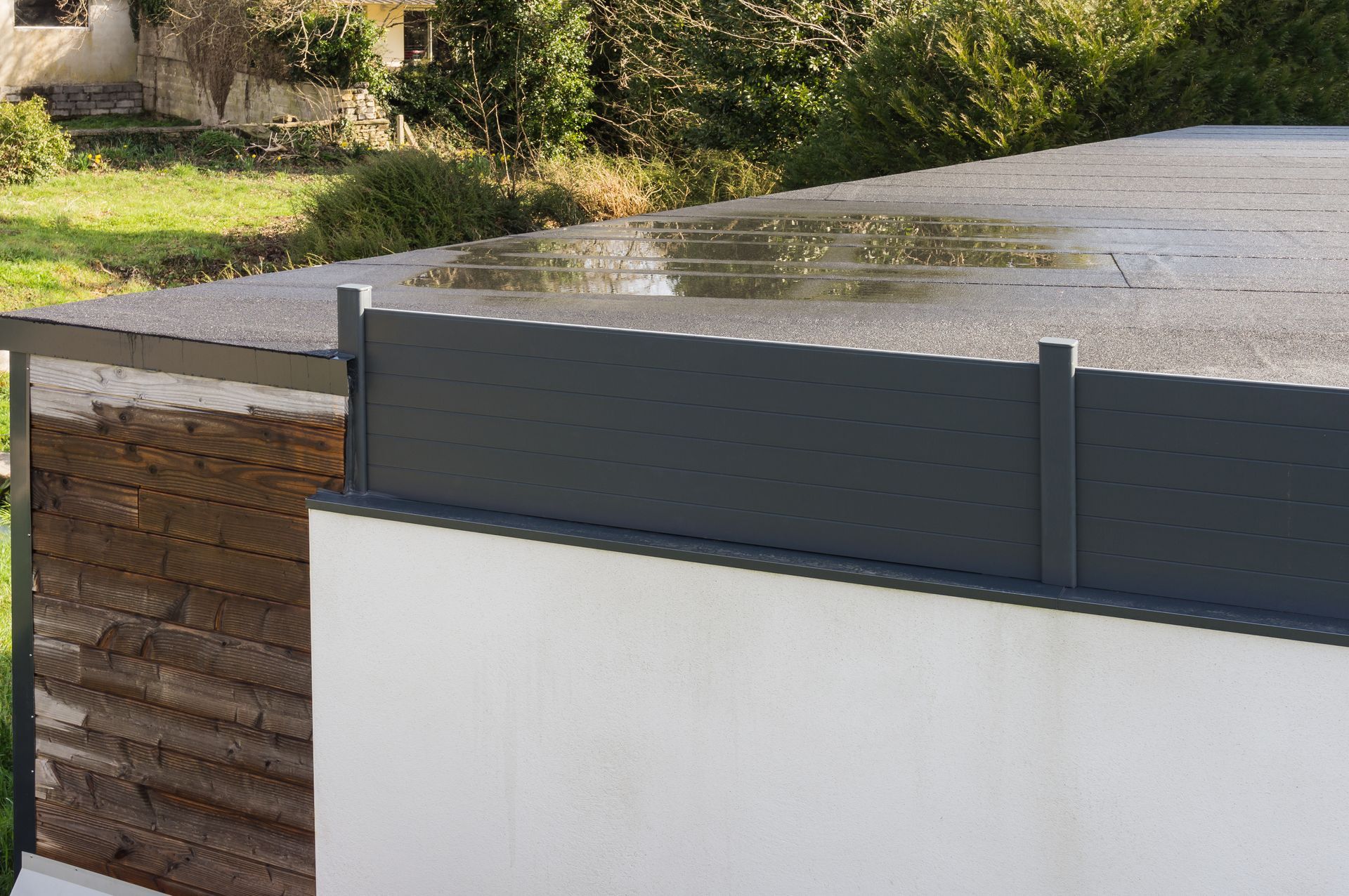 Modern residential fence with gray privacy panels and a white wall beside a wooden gate outdoors