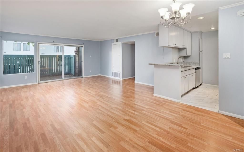 Empty living room with wood flooring, sliding glass door to a patio, and a partially visible kitchen.