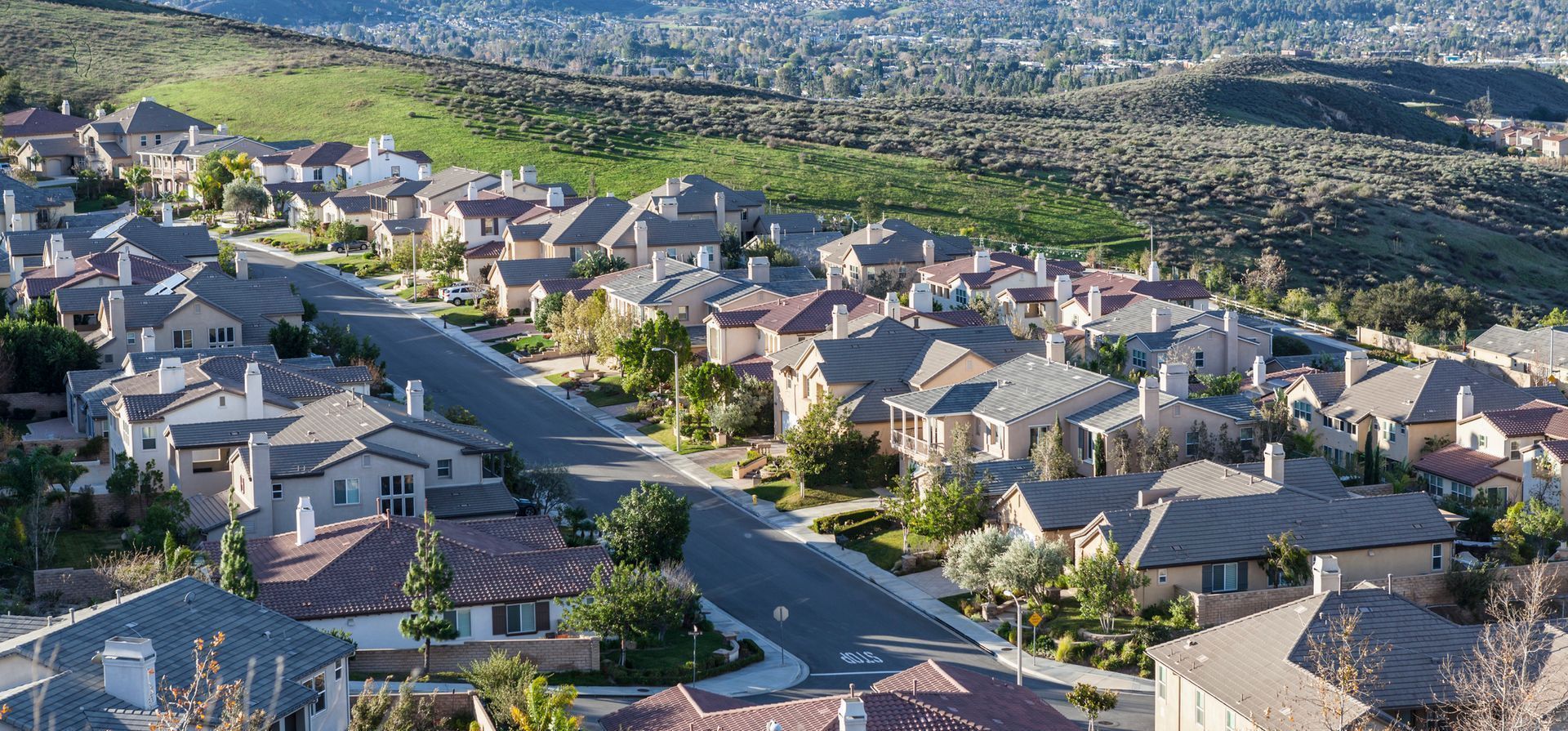 Aerial view of a suburban neighborhood with houses and streets surrounded by green hills.