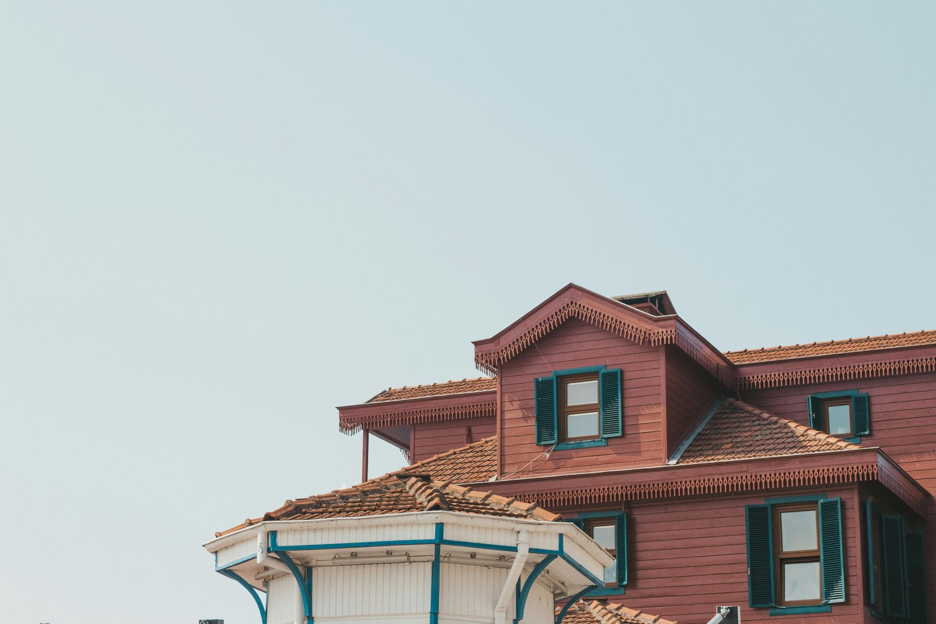 Red wooden house with blue shutters against a clear sky.