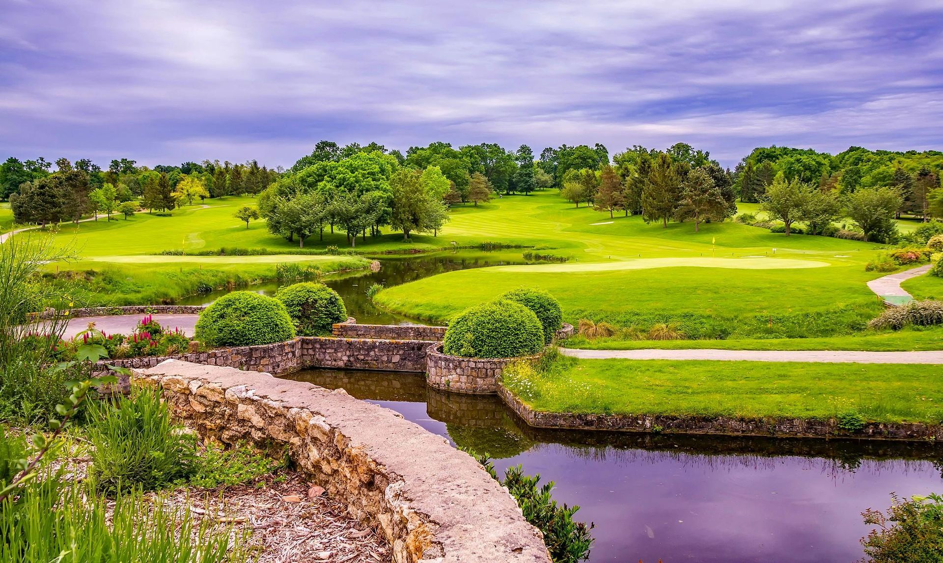 Scenic view of a lush green golf course with a river running through it under a cloudy sky.