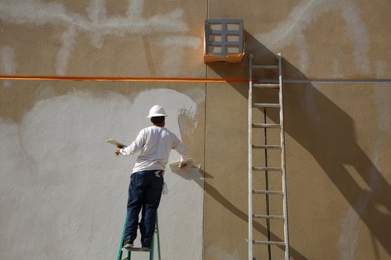 Worker on ladder filling cracks in stucco preparing for paint