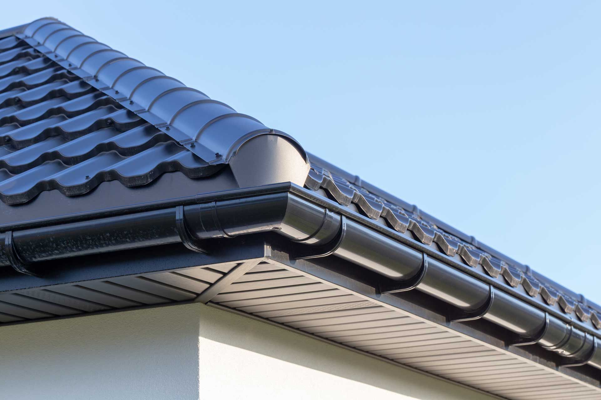 Black roof with matching gutters against a blue sky, close-up view.