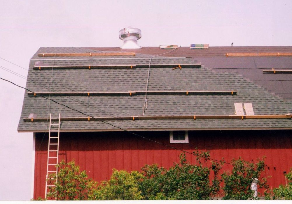 Red barn with gray roof, solar panels being installed. Ladder leans against the side.