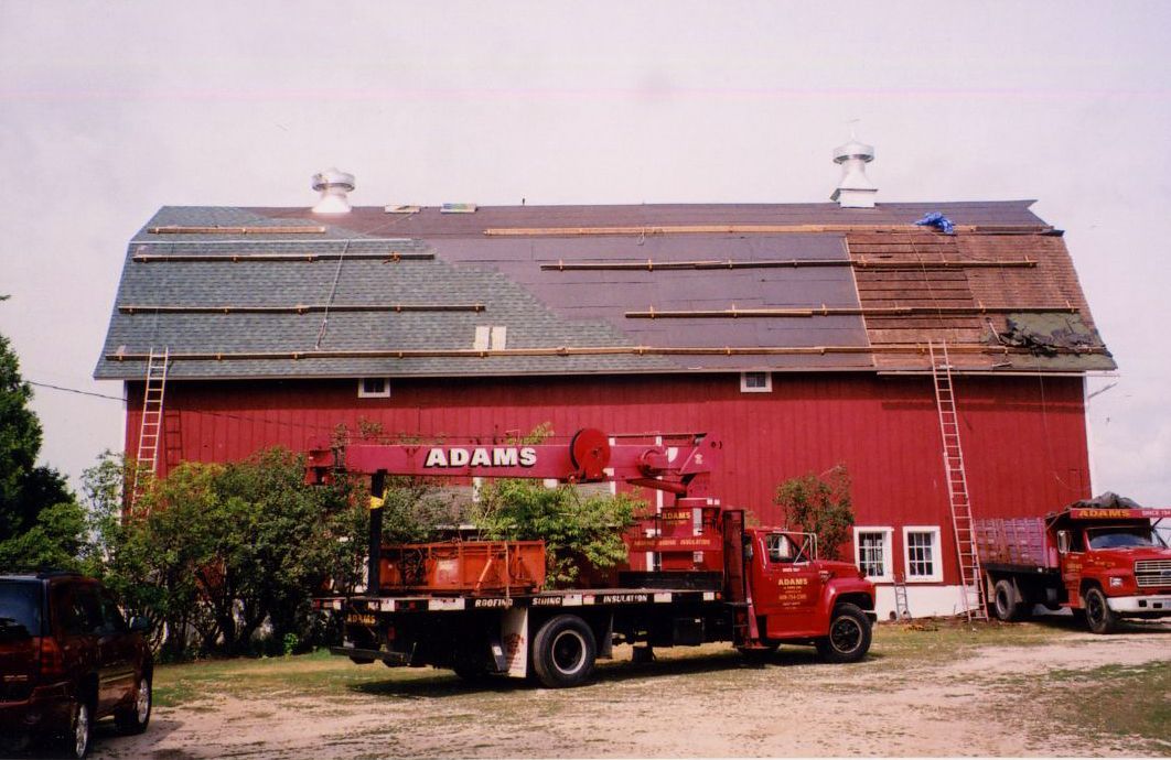 Red barn with roof partially under repair, with a red truck in front.