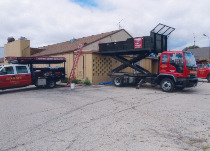 Trucks with lift platforms by a building, likely for repair or maintenance work.