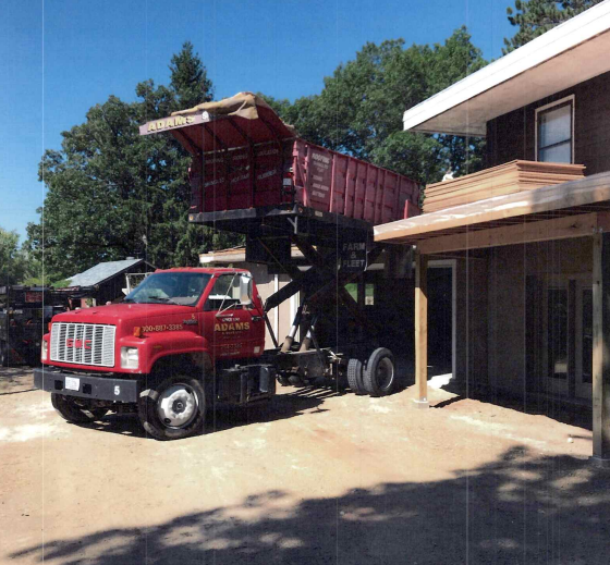 Gray house with a dark roof and white trim, featuring dormers and a patio, set on a green lawn.