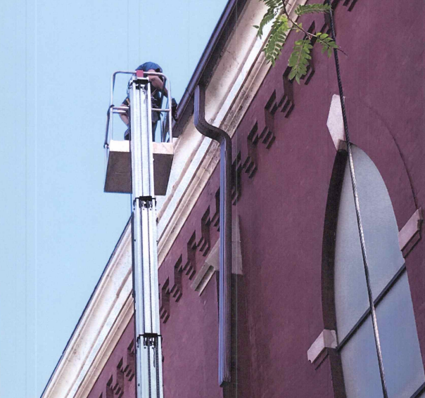 Dark gray gutters and downspout on a white house, against a teal sky.