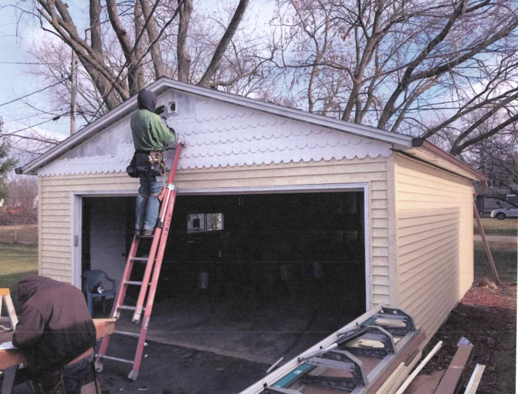 Interior view of attic insulation. Yellow fiberglass batts between wooden studs. A ladder and small window are present.