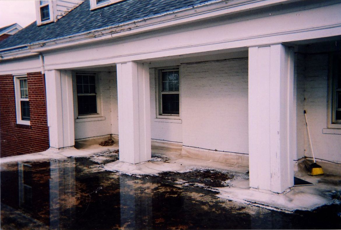 Exterior of a building with a flooded walkway. White columns support a covered porch, snow on the ground.