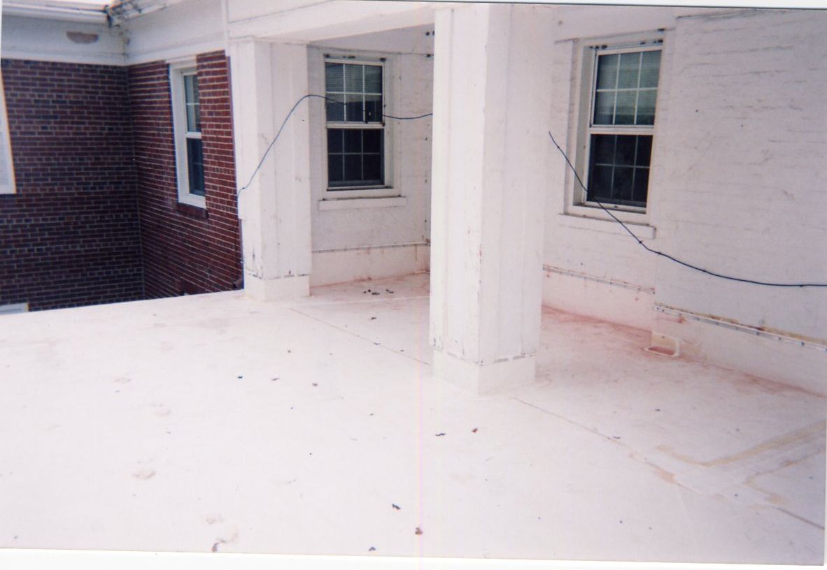 White exterior with brick wall, two windows, and columns.