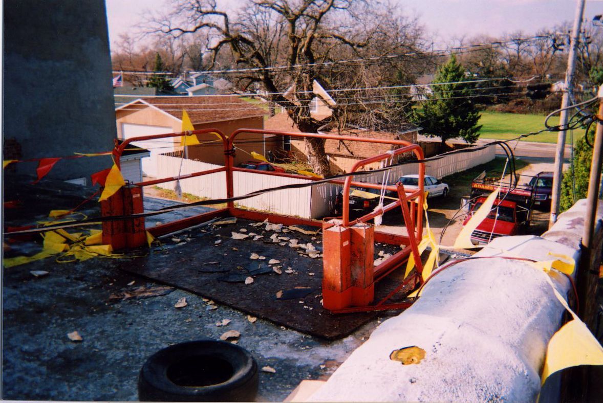Red safety railing on a rooftop with a pipe, with houses and trees visible in the background.