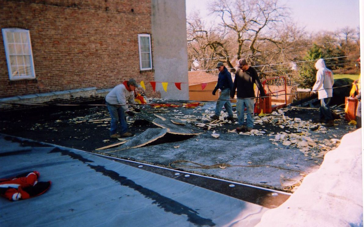 Workers removing roofing material from a building's flat roof on a sunny day.