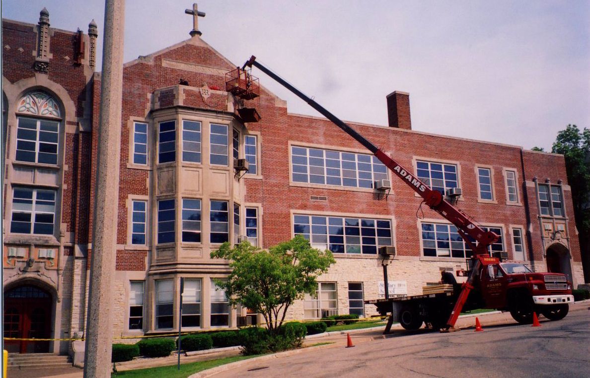 Two-story house with tan siding, white garage door, brown roof, and a clear blue sky.