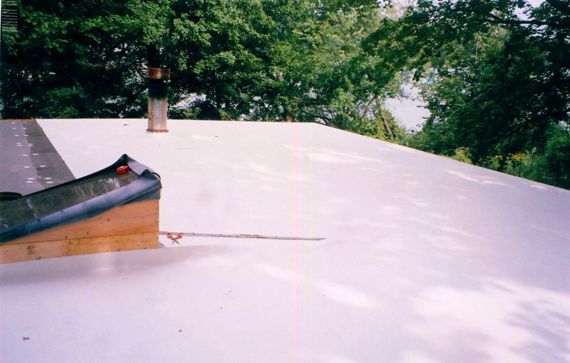 White flat roof with chimney and wooden trim. Trees in background.