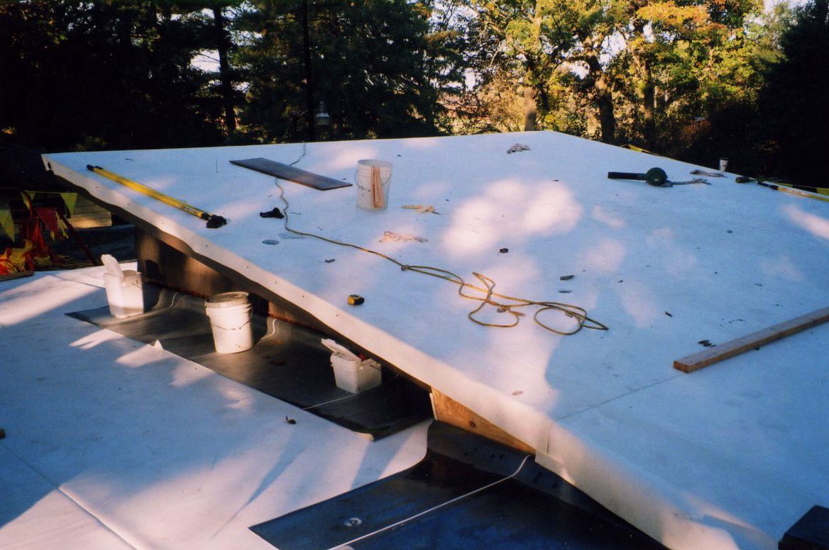 Roof under construction, white insulation panels, tools scattered, outdoors.