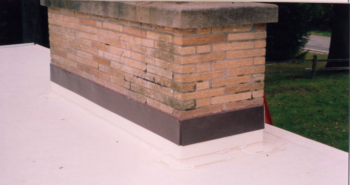 Brick chimney with a metal flashing on a white flat roof.