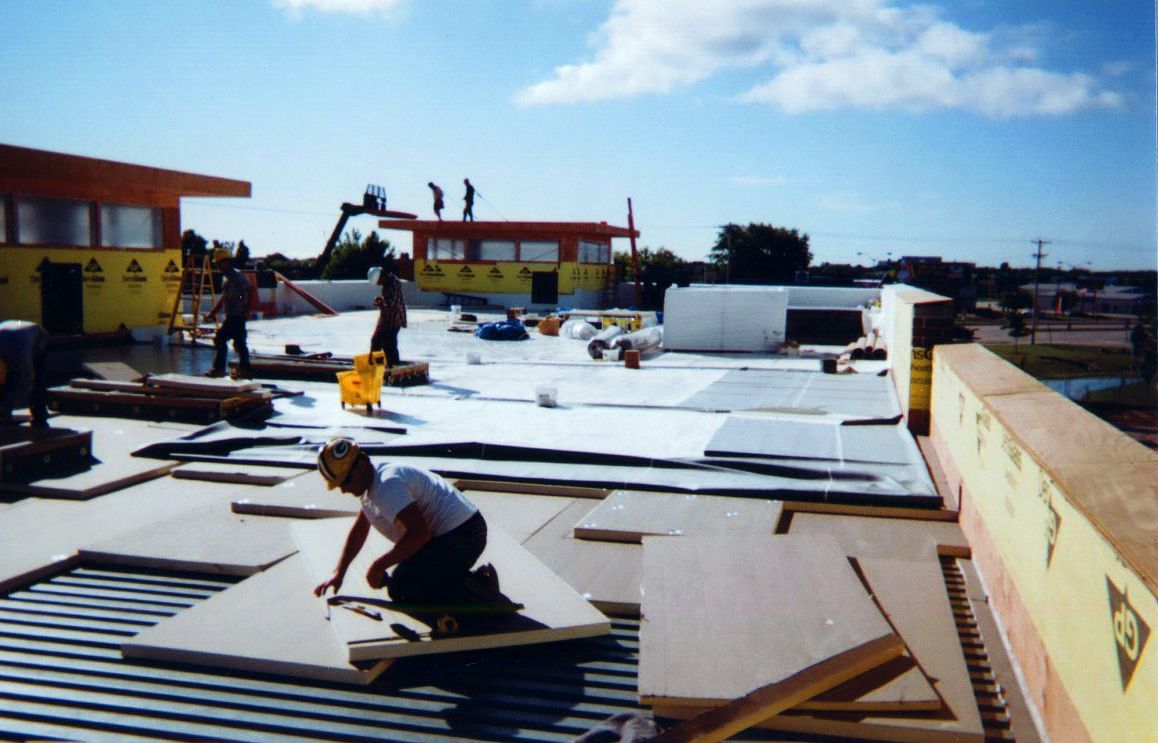 Construction workers on a roof installing insulation and roofing materials on a sunny day.