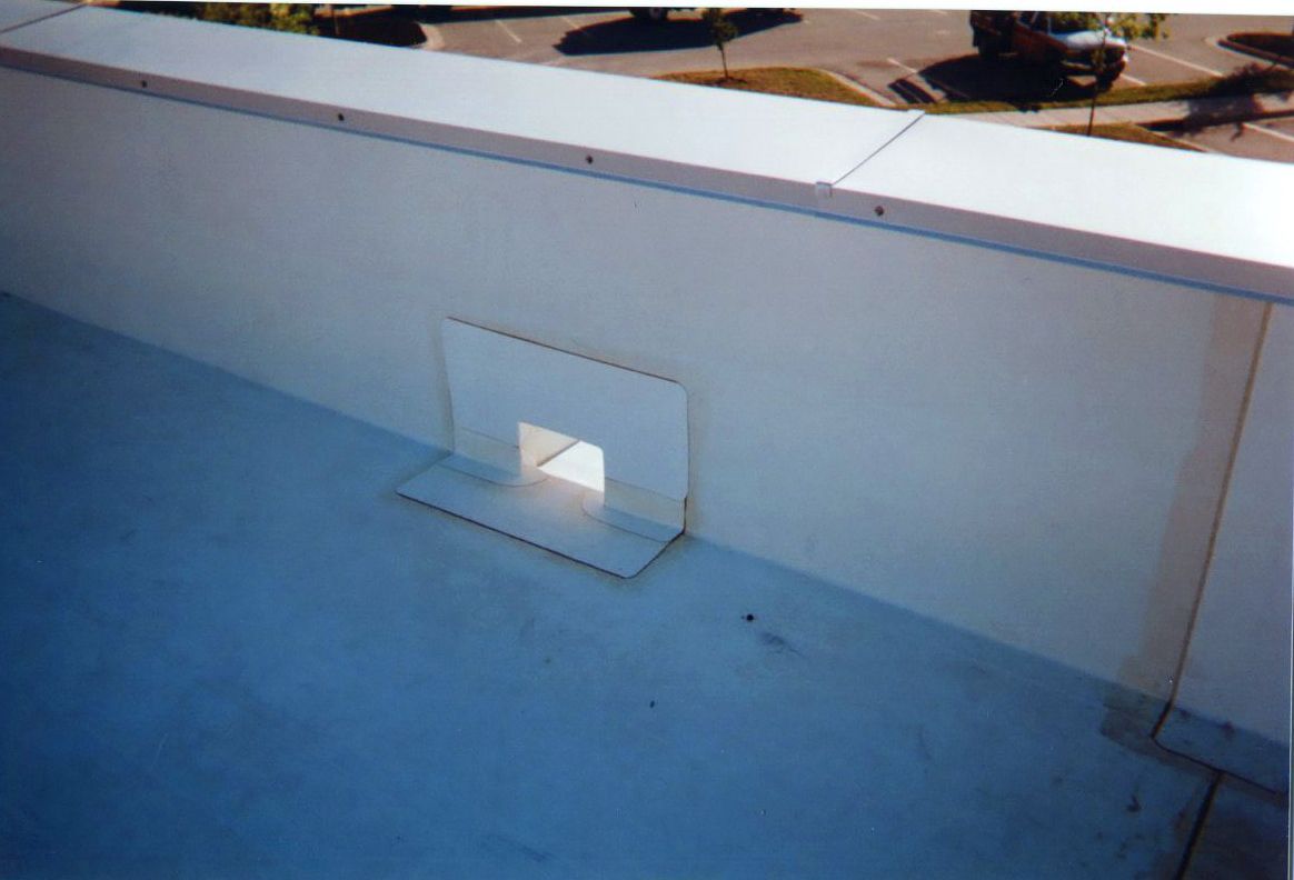 White commercial roof with a drainage outlet, light blue surface, and surrounding white walls.