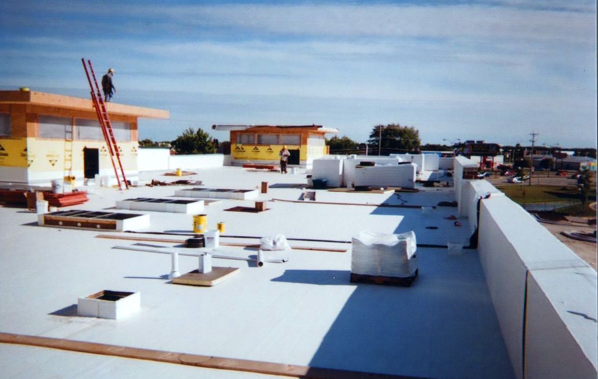 Workers on a flat roof with equipment, under construction; sunny day.