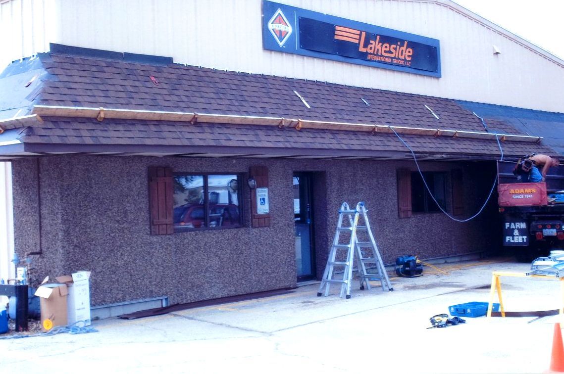 Exterior of a business being worked on; brown stucco facade, ladder, tools, and a truck parked nearby.