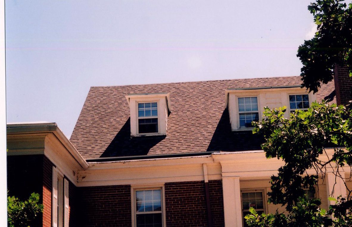 Brick building with a dark roof and three dormer windows under a clear sky.