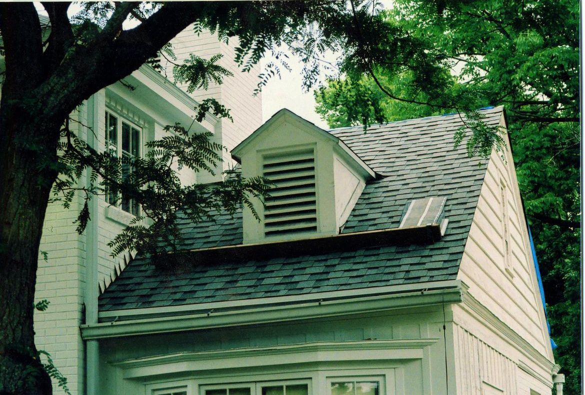 White house with shingle roof, dormer, and trees.