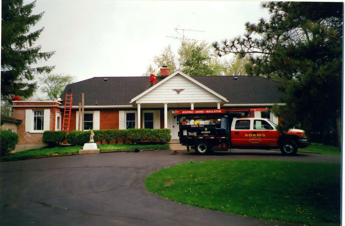 A red pickup truck with equipment parked in front of a brick house with a newly shingled roof.
