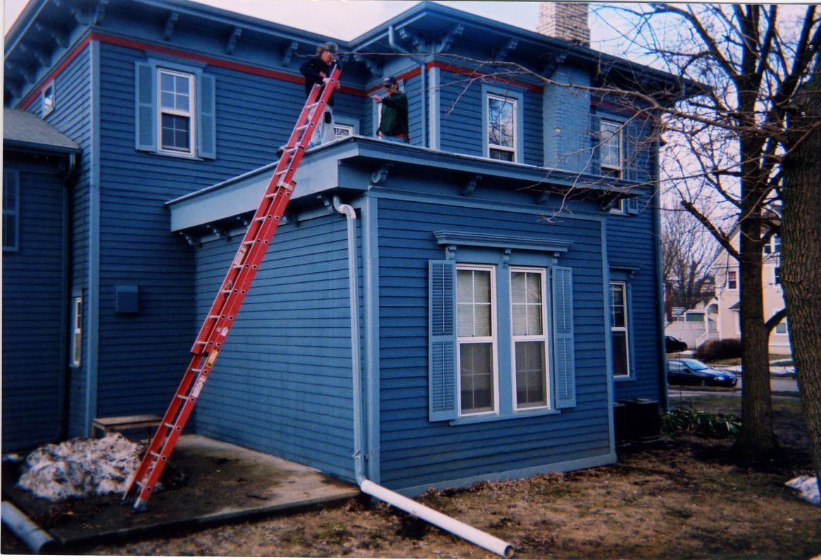 A person on a red ladder working on the blue exterior of a two-story house.