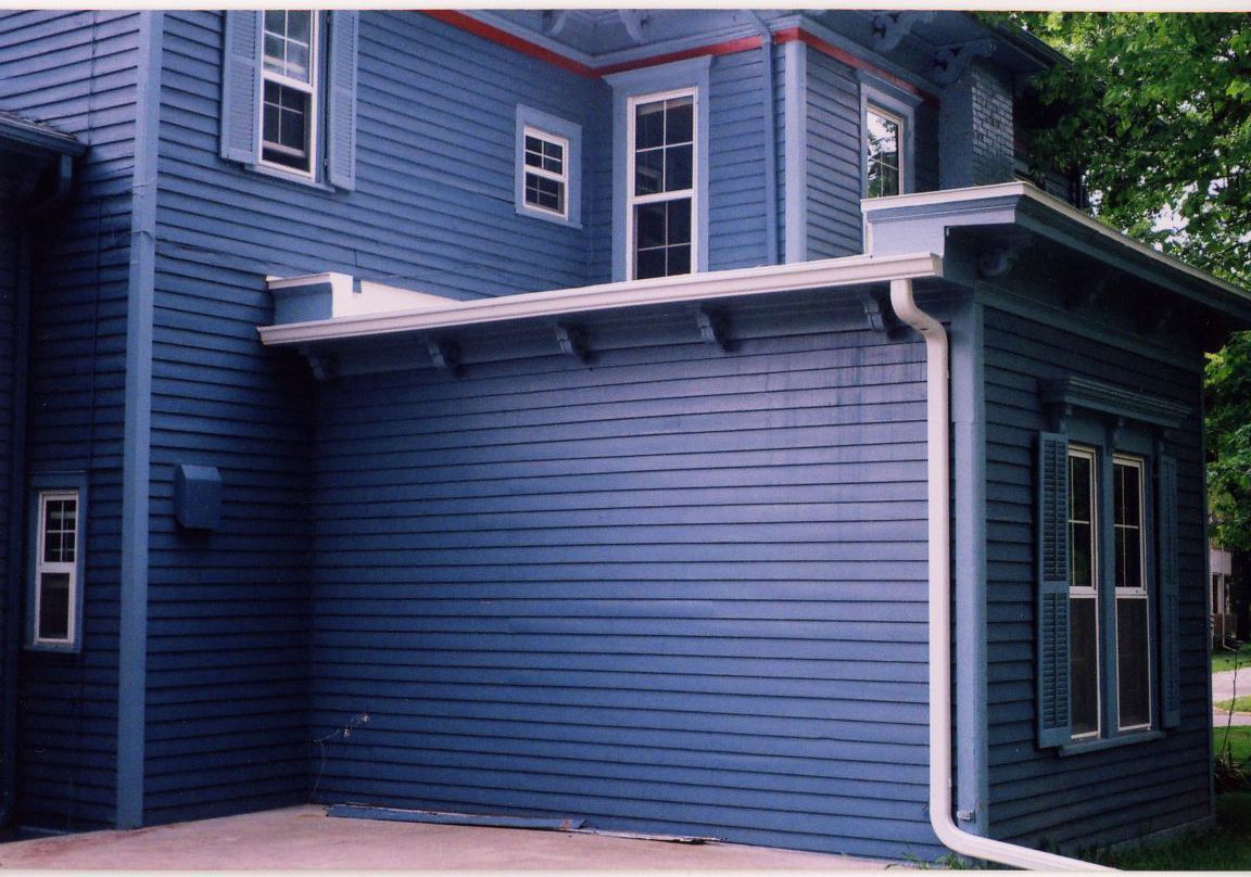 Blue house with windows, shutters, and an attached porch with a flat roof.