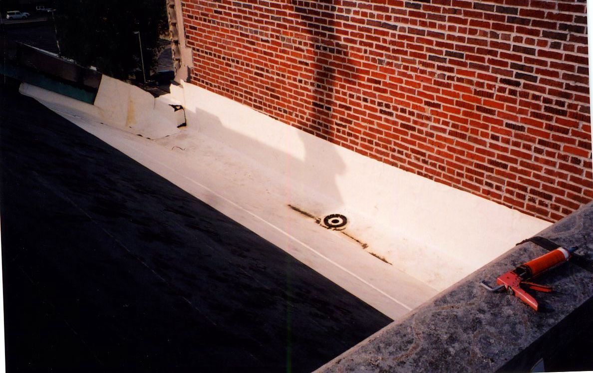 White-painted roof with brick wall on one side. Red caulk gun on gray ledge. Dark shadow in the foreground.