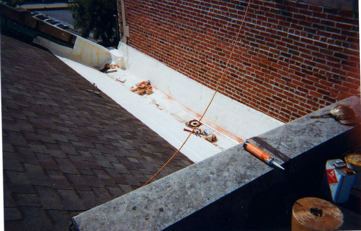 Roof with brick wall, showing white membrane and tools.