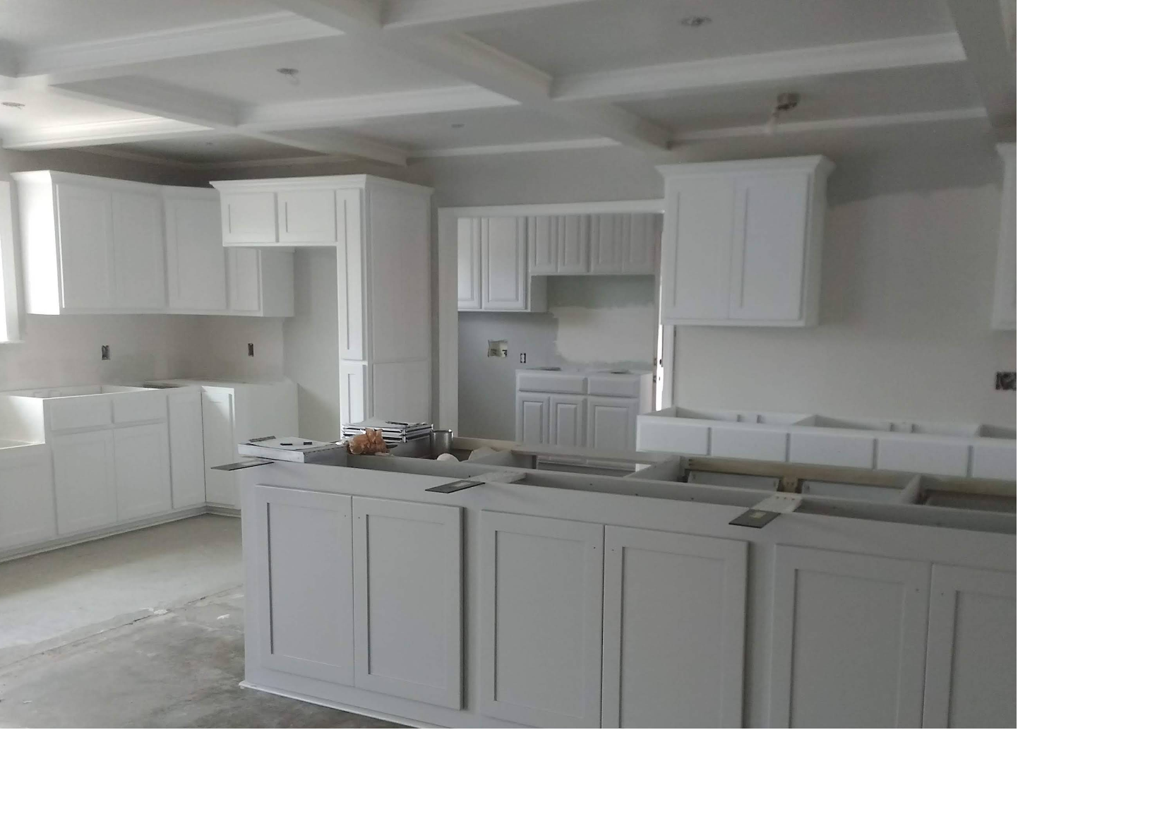 White kitchen cabinets installed in a room under construction; island in foreground.