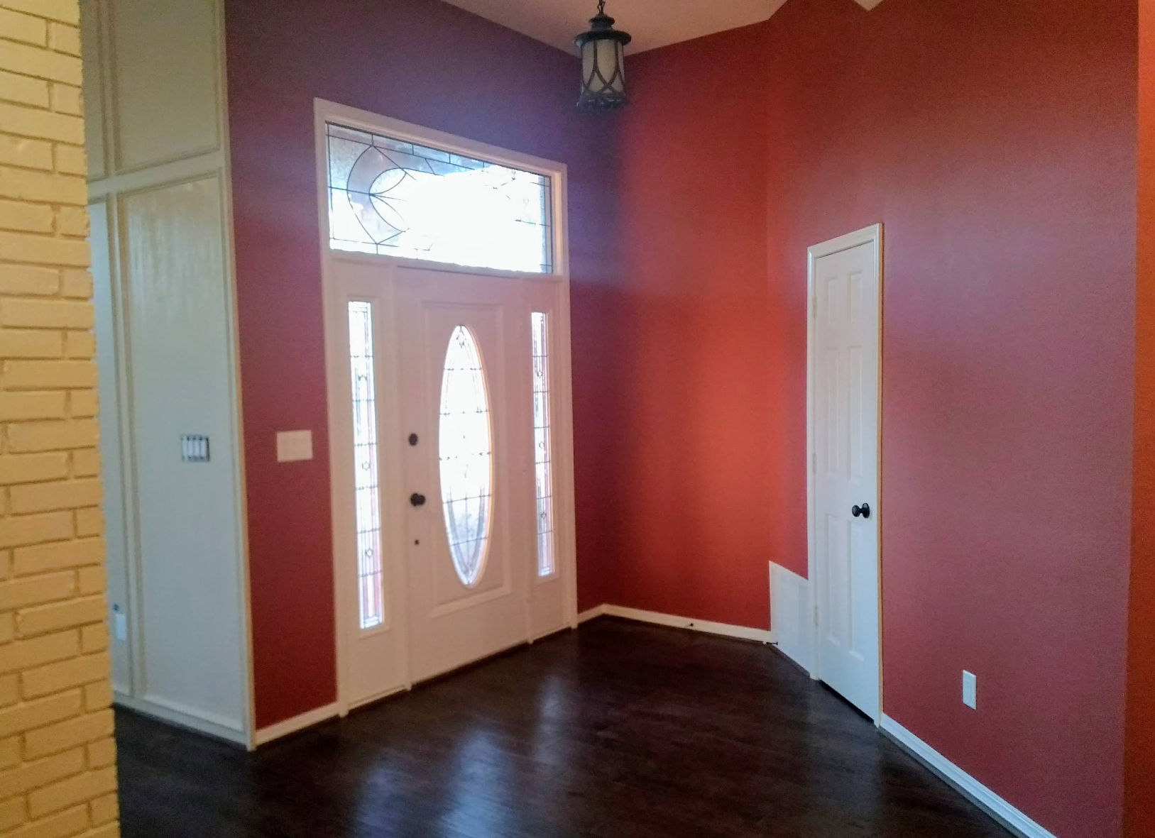 Entryway with a dark wood floor, red walls, white door with stained glass, and overhead light.