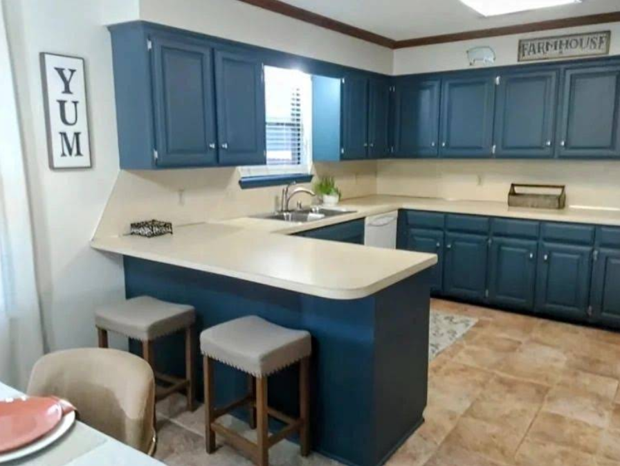 Blue kitchen cabinets with off-white countertops, tile floor, and two stools at a breakfast bar.