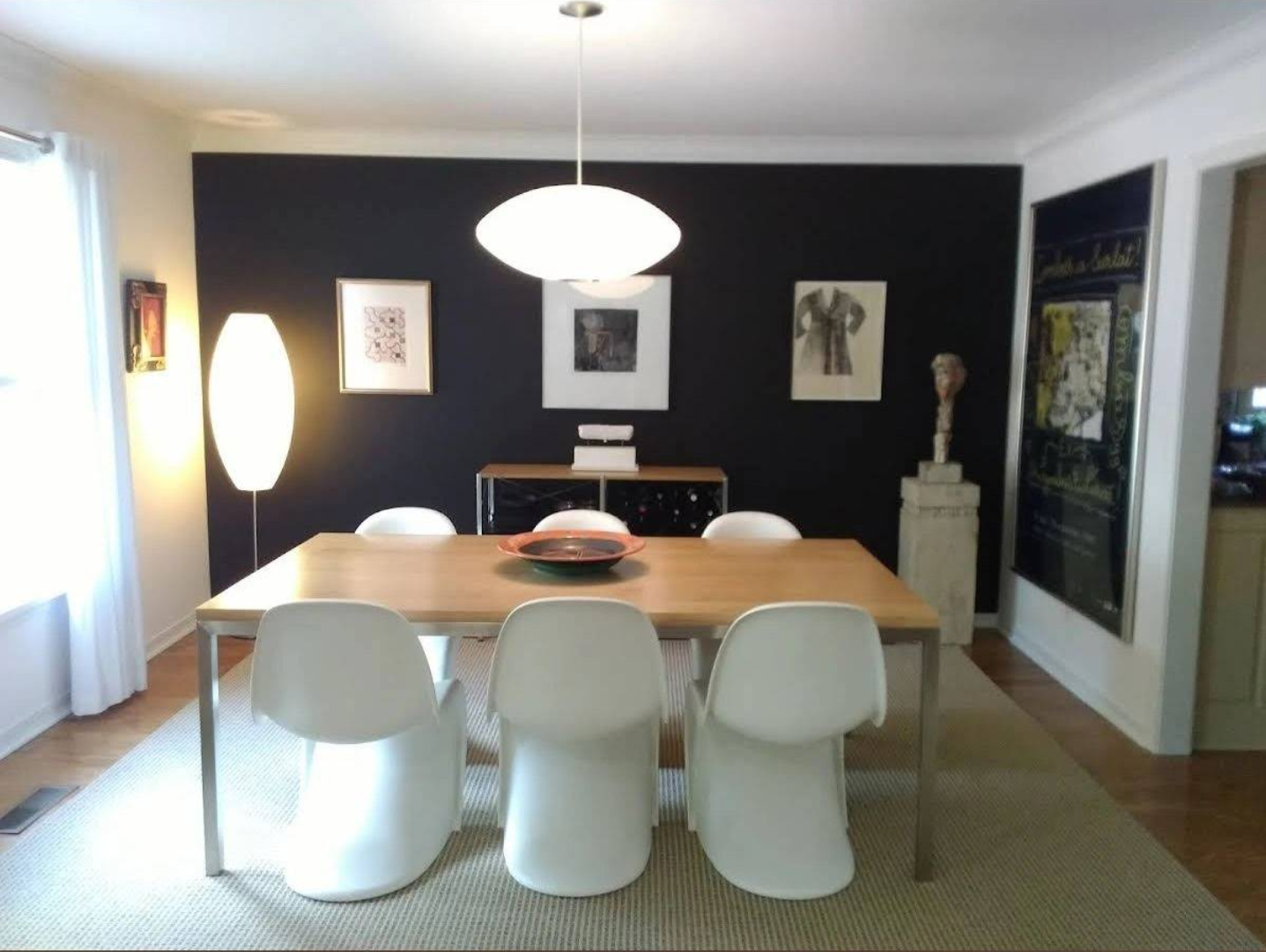 Dining room with black accent wall, white chairs, and a light-colored wooden table.