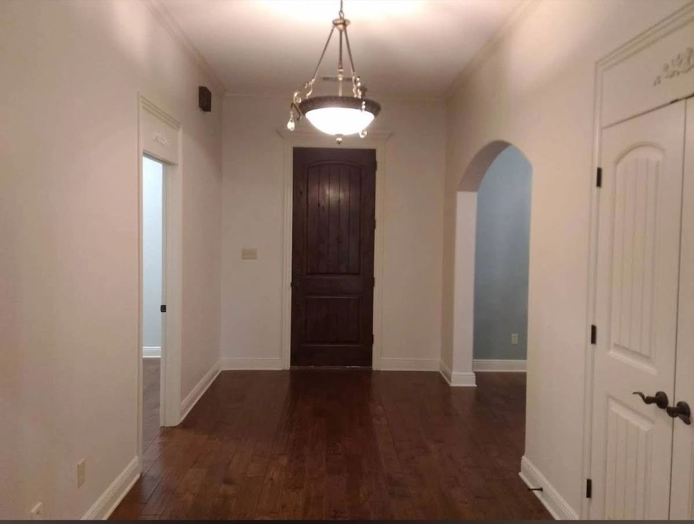 Hallway with dark wooden floor, white walls, dark door, and pendant light.