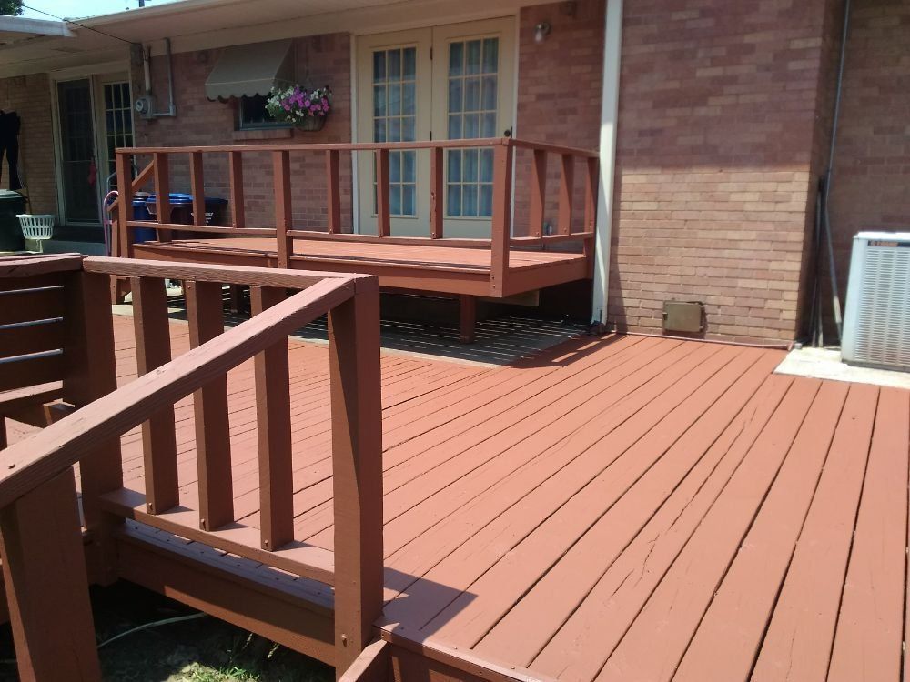 Brown painted wooden deck attached to a brick house with railing and double doors.