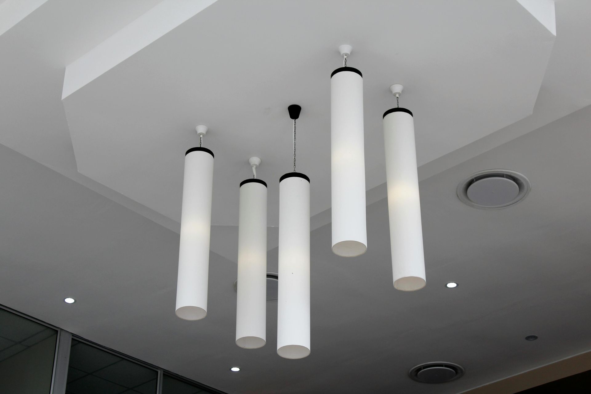 Five white cylindrical pendant lights hang from a white ceiling, with black accents.