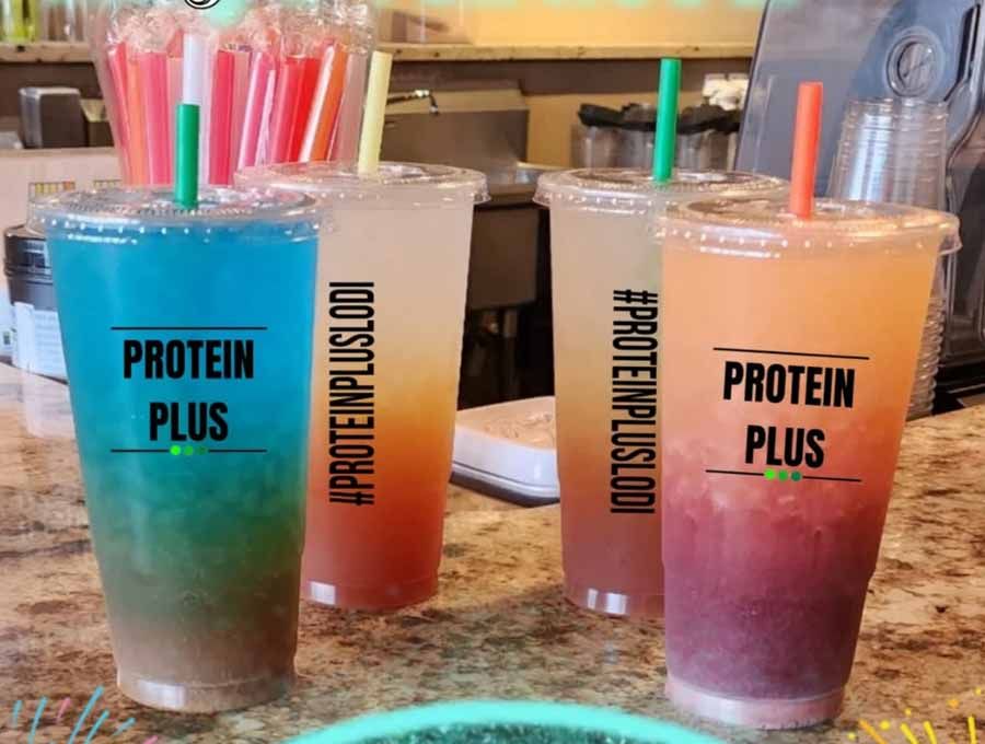 Four colorful Protein Plus drinks with straws, on a counter.