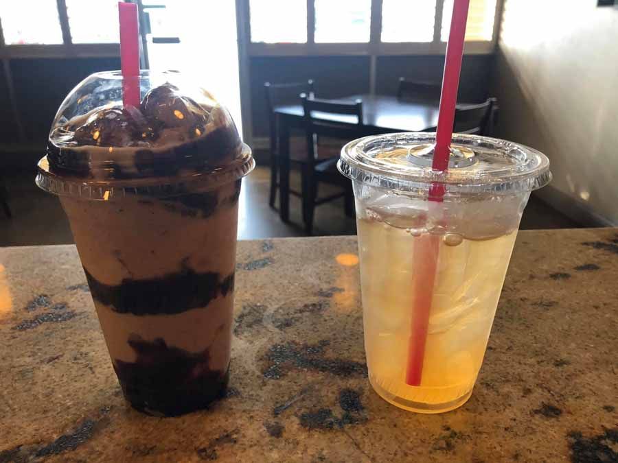 Two drinks on a counter: a layered chocolate shake and a clear drink with a red straw.