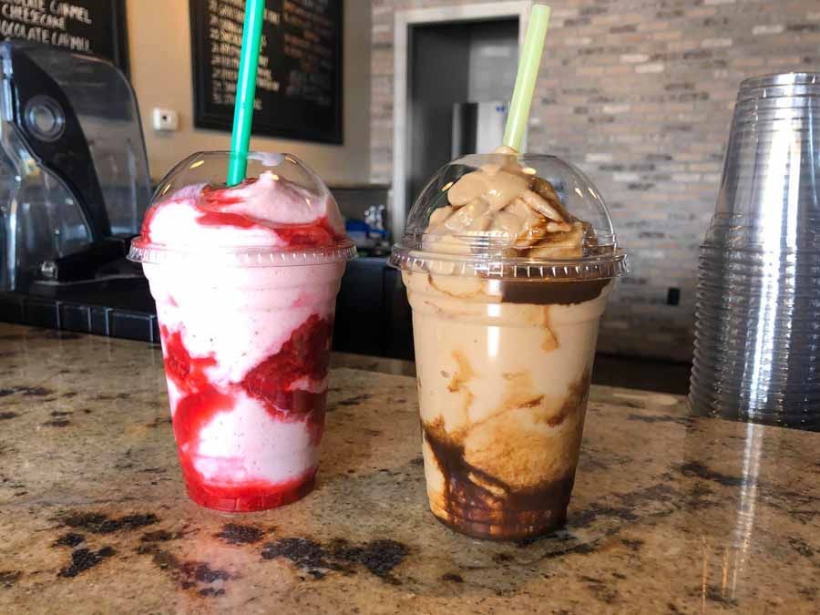 Two blended iced drinks with straws, one strawberry, one coffee, on a counter.