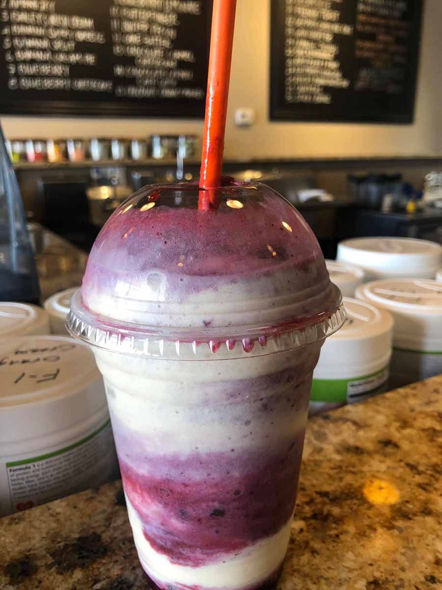 Smoothie in a clear cup with purple and white layers, orange straw on counter.