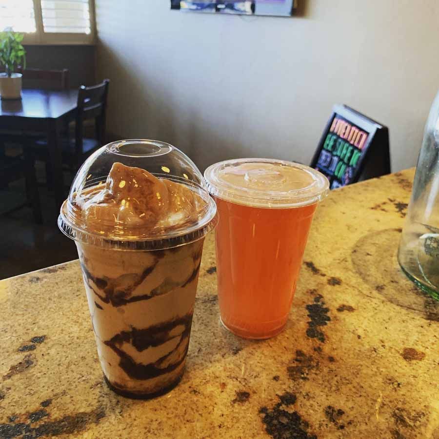 Chocolate smoothie and orange juice in clear cups on a counter at a cafe.