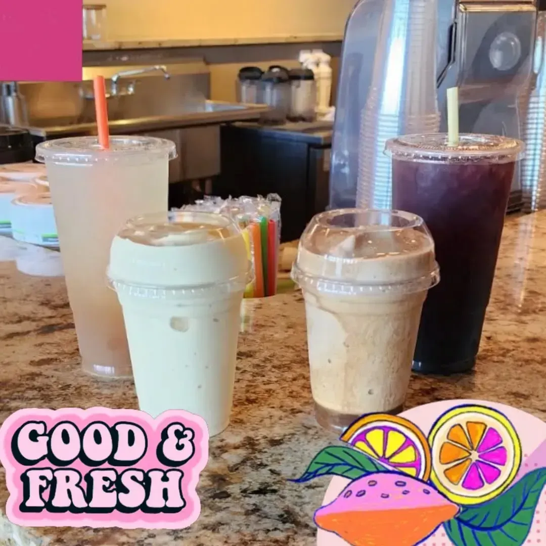 Four colorful drinks in clear cups on a counter: a lemonade, a smoothie, and a purple drink, with a 