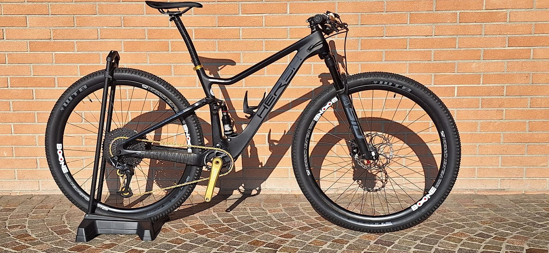 Una bicicletta nera è parcheggiata davanti a un muro di mattoni.