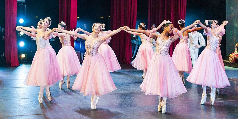 Um grupo de bailarinas em vestidos rosa estão dançando em um palco.